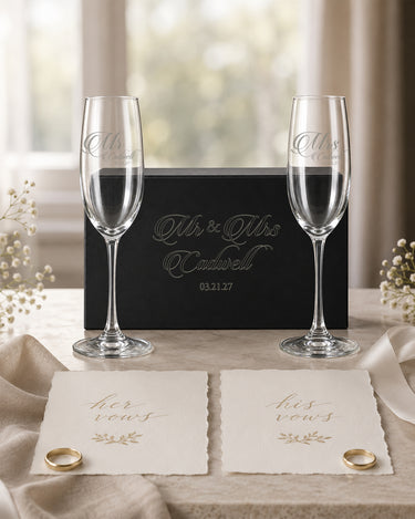 Two personalized champagne flutes with Mr and Mrs script titles, a shared surname and date beside a matching black gift box in a wedding scene.