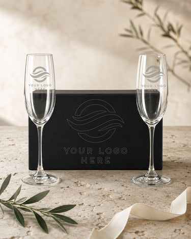 Two custom logo champagne flutes beside a black magnetic box with matching outline artwork on its lid.