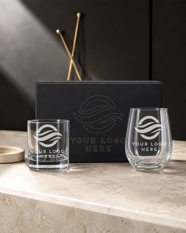 Custom logo rocks glass and stemless wine glass beside a black magnetic box with outline artwork on its lid.