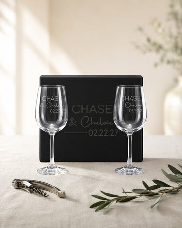 Stemmed Wine Glasses with two names in print and script, a divider and date beside a matching engraved black magnetic gift box.