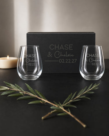 Stemless Wine Glasses with two names in print and script, a divider and date beside a matching engraved black magnetic gift box.