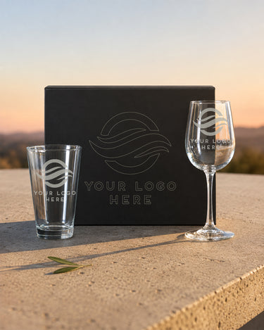 Custom logo pint and stemmed wine glasses beside a black magnetic gift box with outline artwork on the lid.
