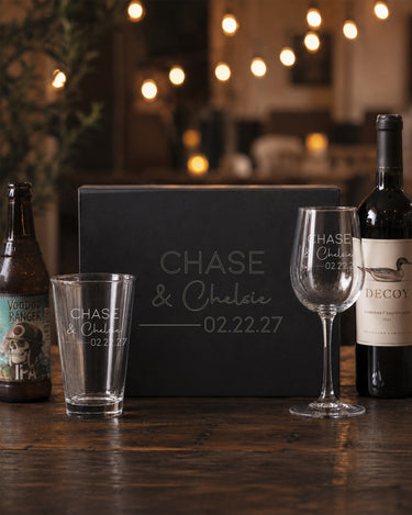 Pint and Stemmed Wine Glass Set with two names in print and script, a divider and date beside a matching engraved black magnetic gift box.