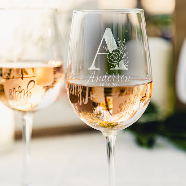 Stemmed wine glass with etched design. The design has the initial A with a floral design on it and with the name Anderson underneath in a script font and the date in a smaller size below that in a print font.