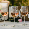 Stemmed white wine glasses with etched anniversary design. The design has a floral border with 5th, 10th, and 15th Anniversary inside the border along with two names for a couple and a wedding or anniversary date.
