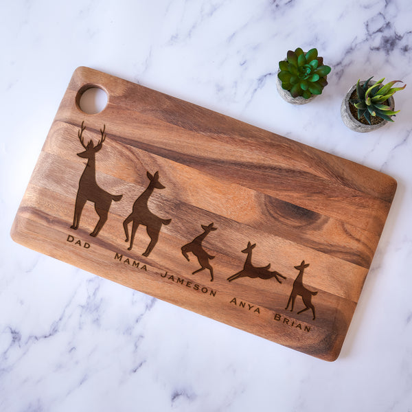 Engraved wood block cutting board. The engraving is on the front and towards the lower bottom part of the board. The engraving is of a family of deer lined in a row. There is a dad deer, mom deer and three kids. Under each deer has a printed name "Dad, Mama, Jameson, Anya, Brian". Deer can be added or taken away.