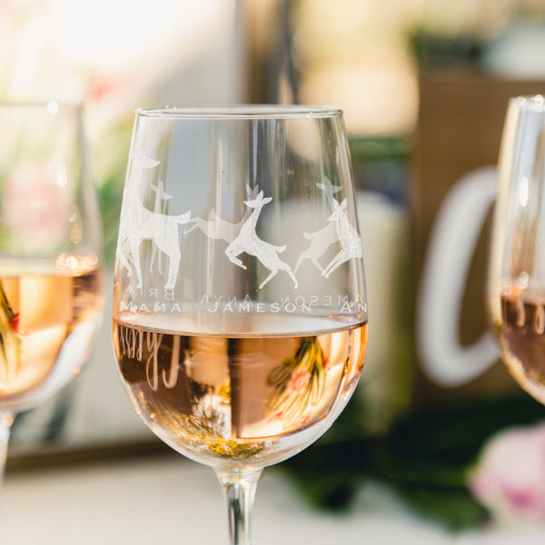 Etched stem white wine glass. The etching wraps around the glass. The design is of a family of deer lined in a row. There is a dad deer, mom deer and three kids. Under each deer has a printed name "Dad, Mama, Jameson, Anya, Brian". Deer can be added or taken away.