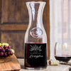 Glass wine decanter on a table. The etched design is centered on the board. The design is of a bouquet of flowers and beneath it is "Alex" and beneath that is "& Madeline" and beneath that is "Livingston". So, three lines of text: first name, send name and a last name.