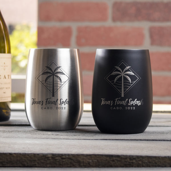Two metal wine tumblers on a table. One tumbler is black and the etched design is in silver. The other tumbler is silver and the etched design is black. The design etched on the tumblers is diamond shape line and dots, inside is a palm tree and waves. Below the design is "Tina's Final Splash" in cursive font, and below that is "CABO, 2022" in printed font. The design is centered on the cup.