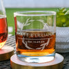 Whiskey glass, with an etched design centered. The design is a circle wreath, in the middle are two lines breaking up the wreath and has MATT & LILLIANA in printed font all caps. Still inside the wreath, and below the names is EST. 10.25.22