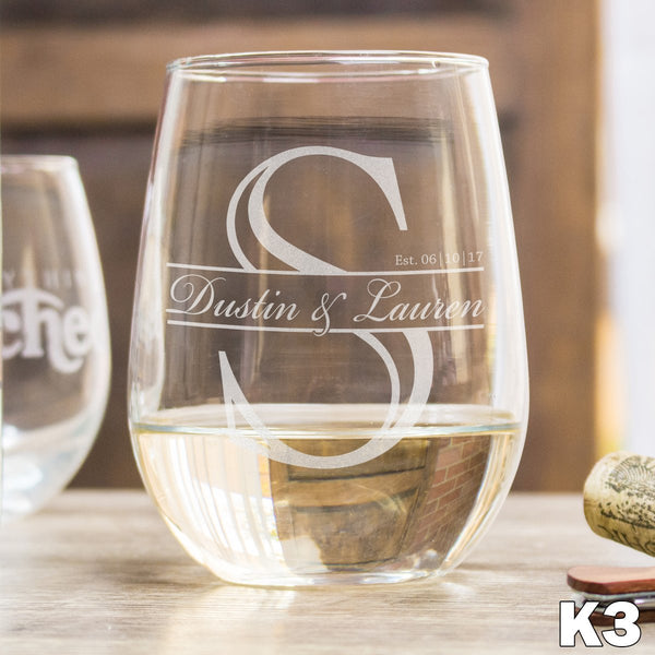Stemless white wine glass with an engraved design in the center. The design has a large initial S with a section in the middle where it has a couple's names in a script font. A date is engraved to the top right of the names